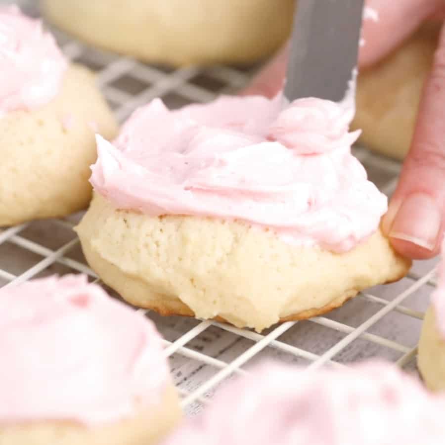 frosting pink vanilla buttercream onto Soft Baked Frosted Vanilla Sugar Cookie Recipe