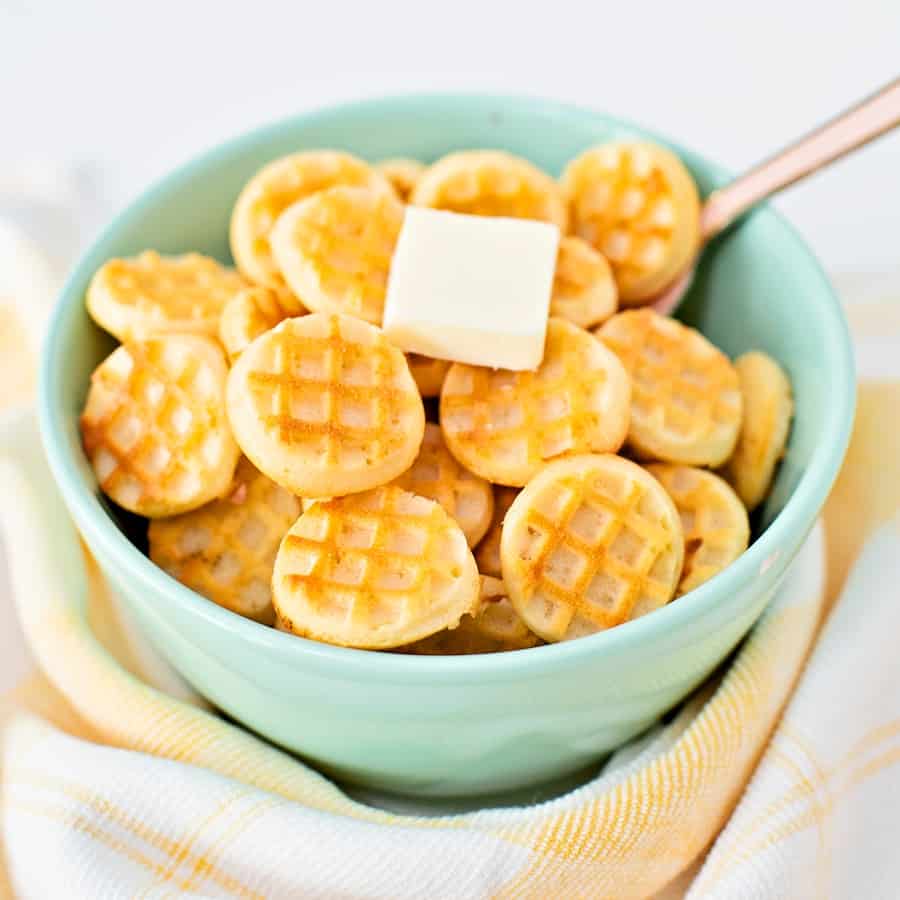 mini waffles in a blue green bowl with a pat of butter on top with a pink spoon inside