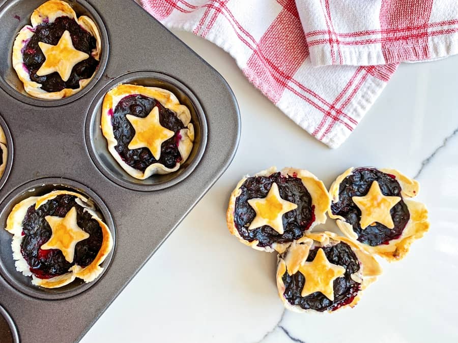 mini berry pies in a muffin tin with pie dough stars over them