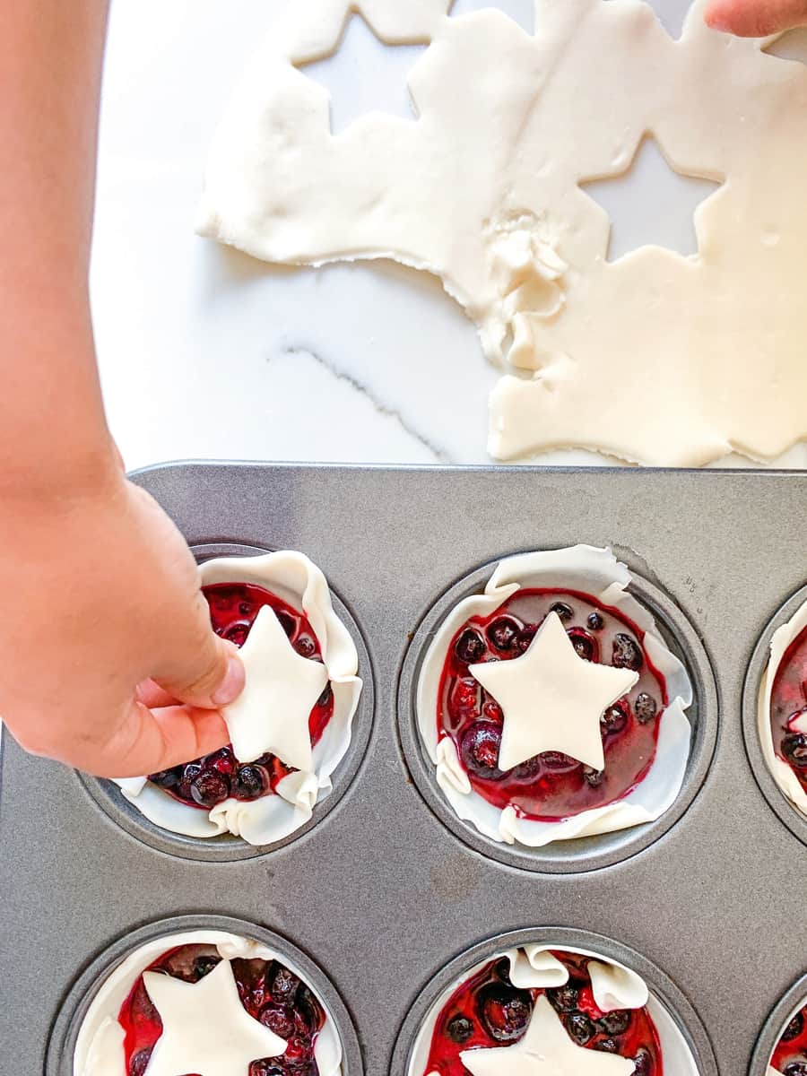 placing a cut pie dough star over mini berry pies in a muffin tin