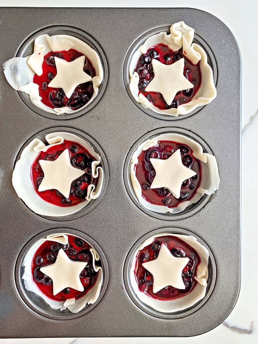mini berry pies in a muffin tin with star pie dough over them