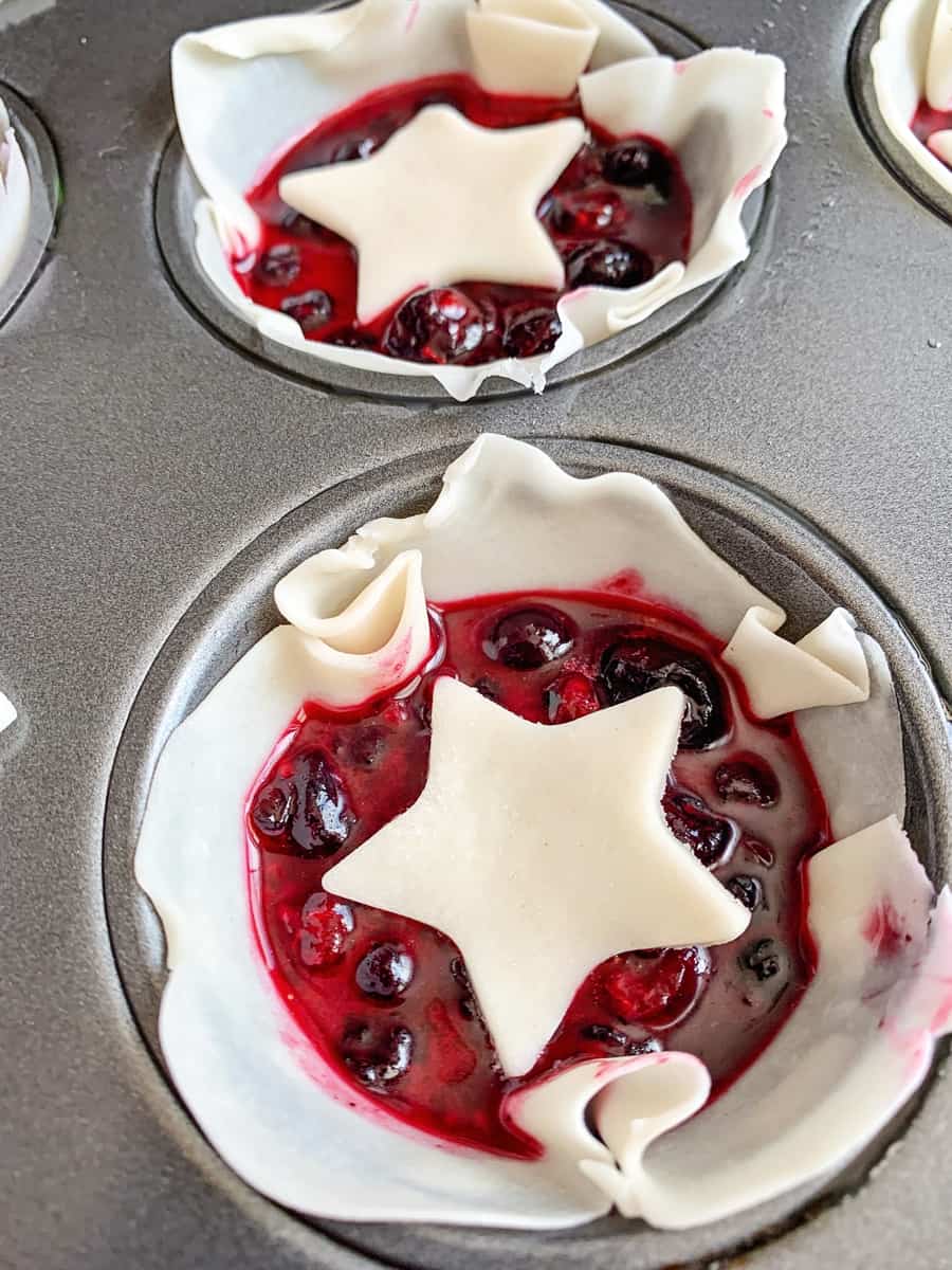 mini berry pies in a muffin tin with star pie dough over them