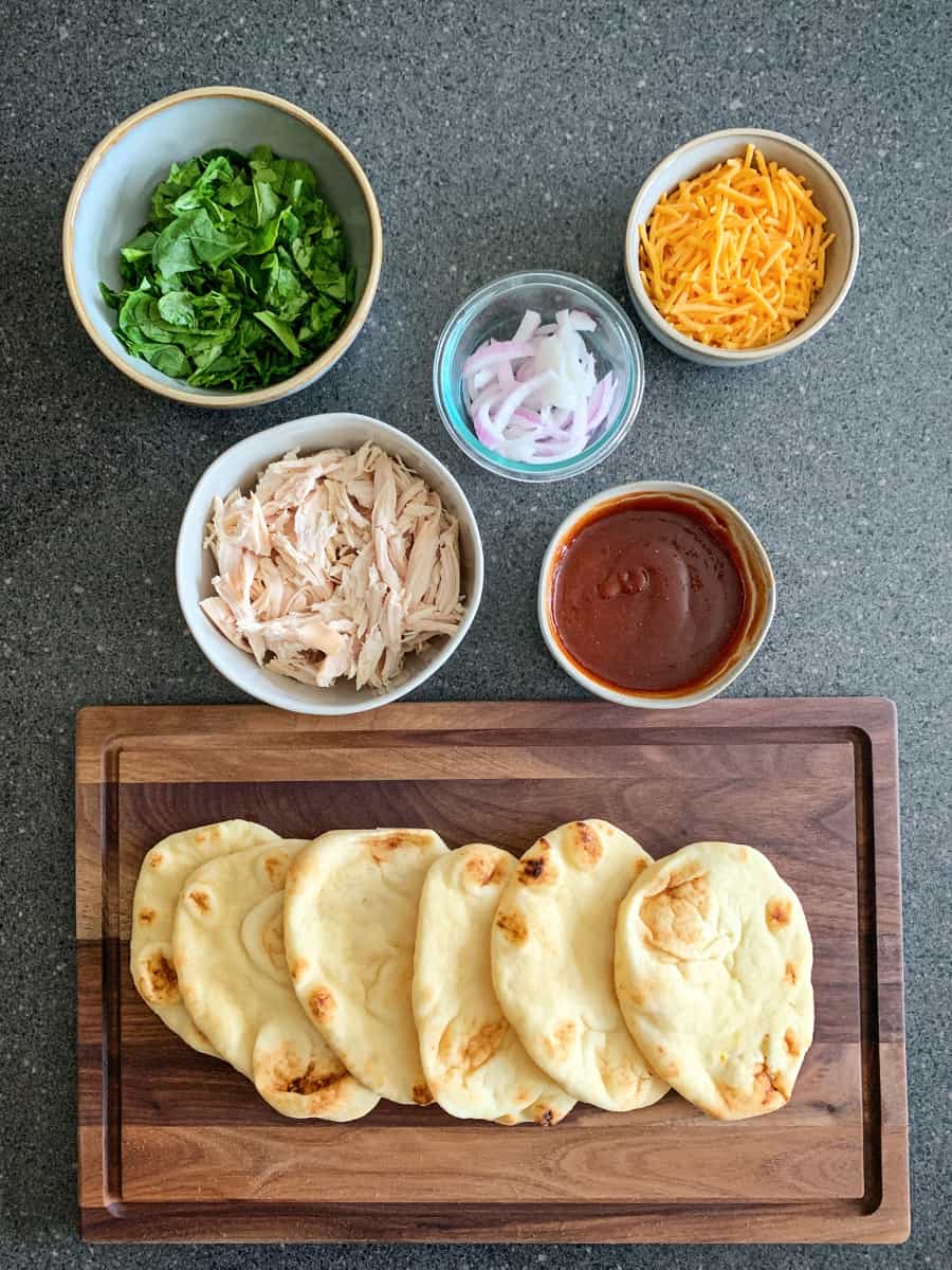 mini naan bread with toppings like chicken, spinach, cheese, bbq sauce and onions