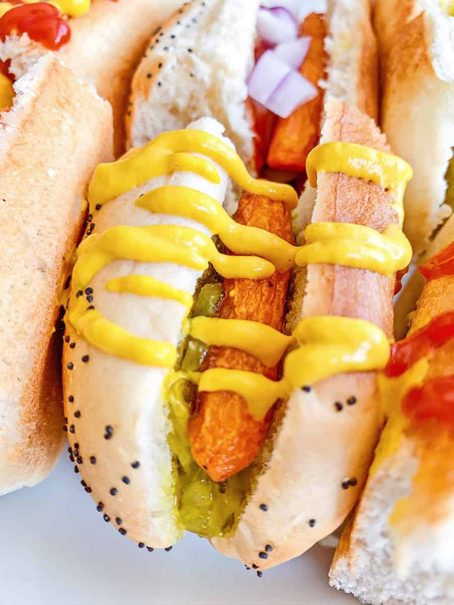 carrot hot dogs on sliced half buns with various hot dog toppings like mustard, ketchup and relish