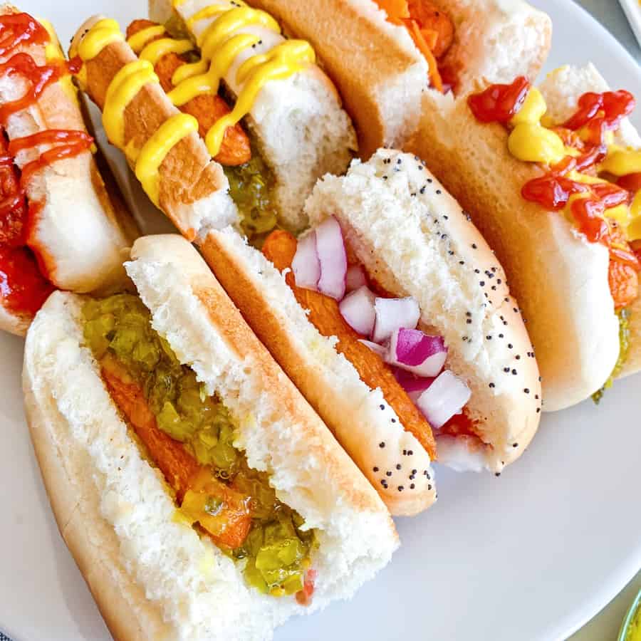 carrot hot dogs on sliced half buns with various hot dog toppings like mustard, ketchup and relish