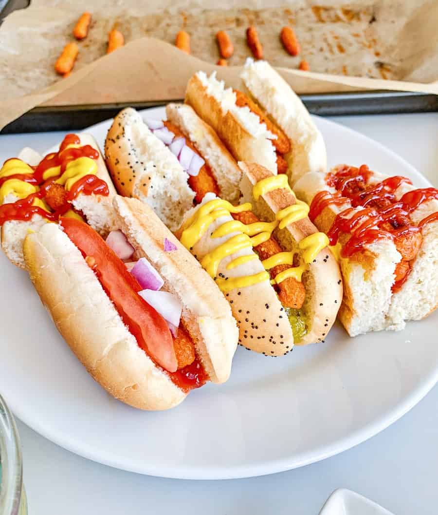 carrot hot dogs on sliced half buns with various hot dog toppings like mustard, ketchup and relish