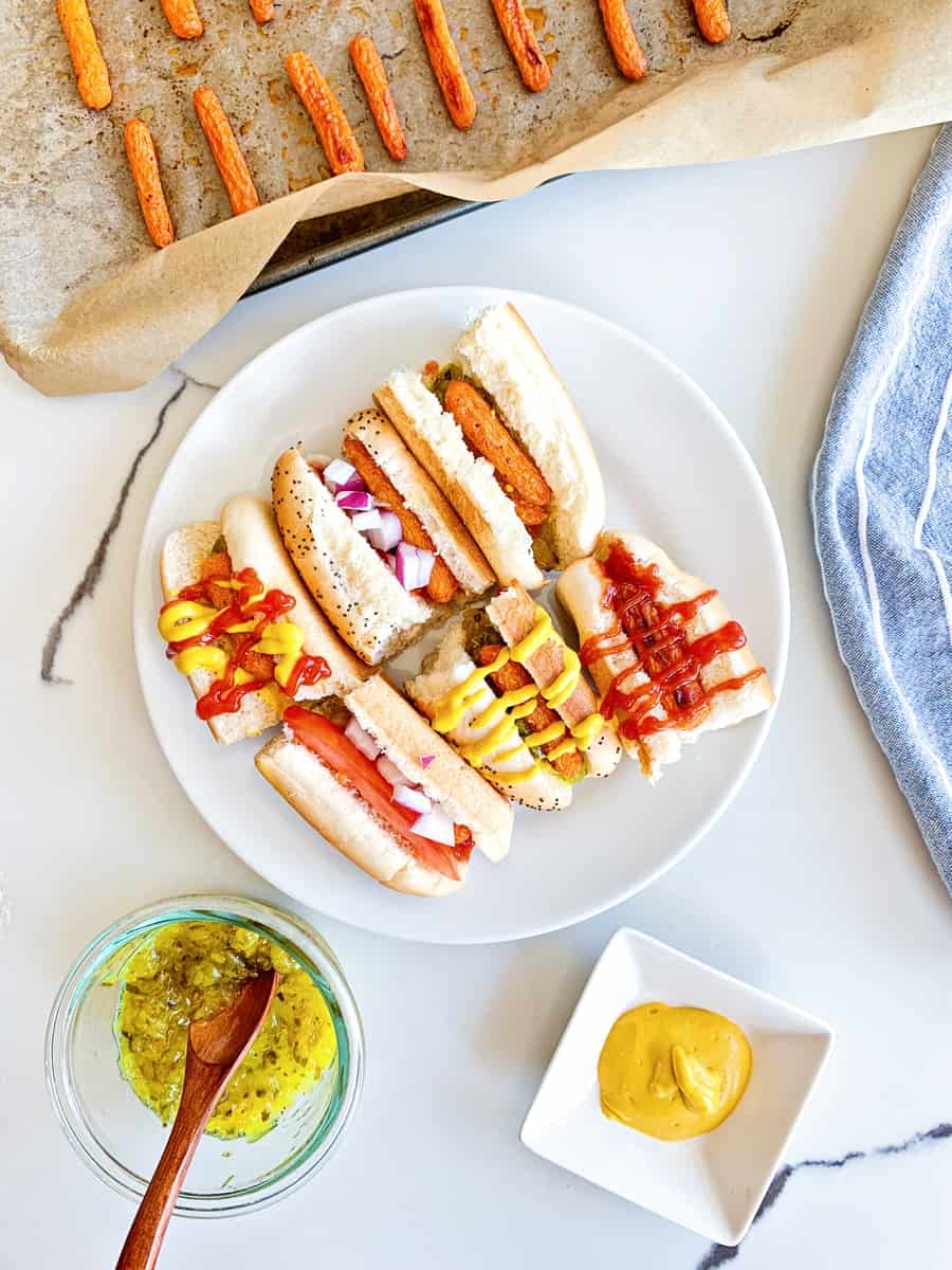 carrot hot dogs on sliced half buns with various hot dog toppings like mustard, ketchup and relish