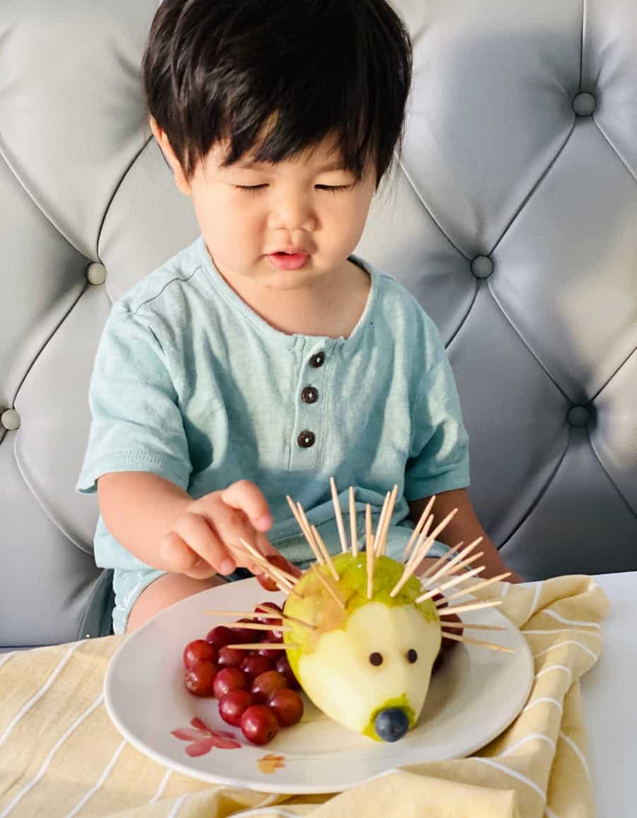 toddler boy practicing fine motor skills on a pear hedgehog made of grapes
