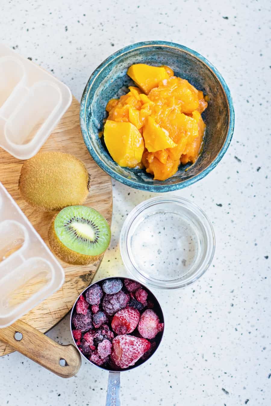 ingredients to make fresh fruit mango popsicles like pureed mango, frozen berries and kiwi fruit 