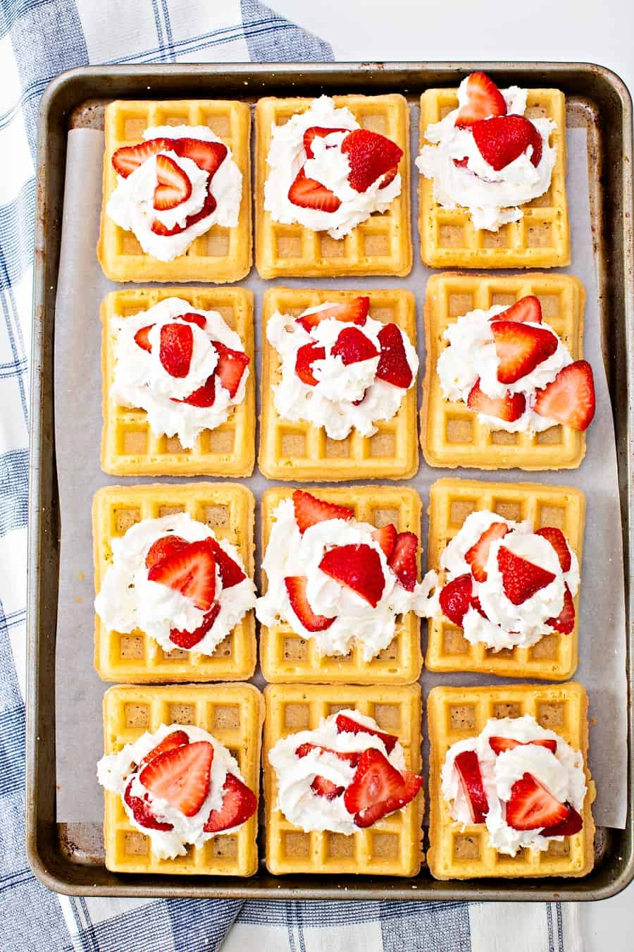 waffles on a sheet pan with whipped cream and strawberries on top