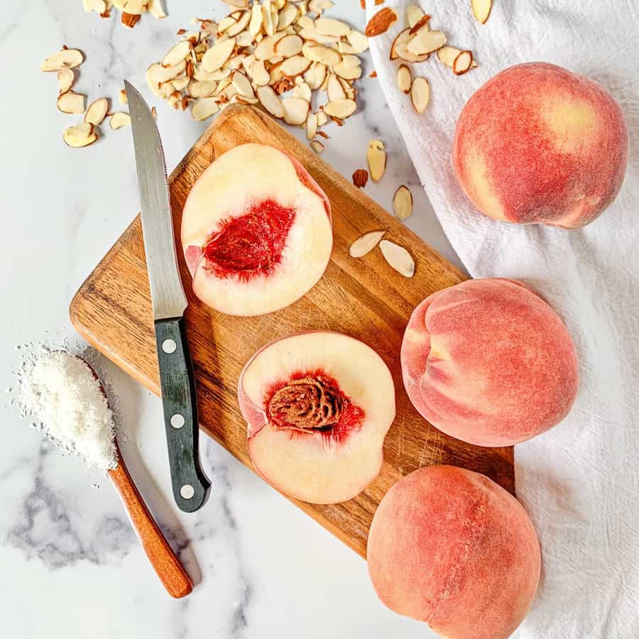 cut peaches on a wooden cutting board with almonds and coconut