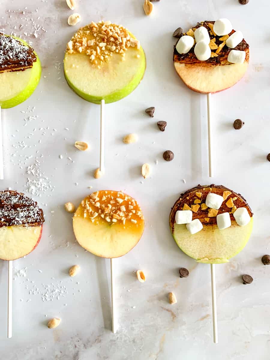 apple fruit lollipops. sliced apples with lollipop sticks and various chocolate, caramel and nut toppings