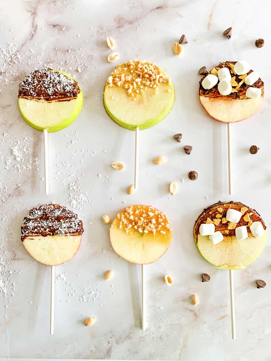 apple fruit lollipops. sliced apples with lollipop sticks and various chocolate, caramel and nut toppings